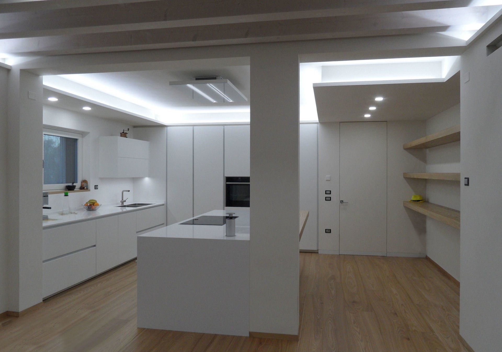 Ambiente cucina con isola dal design moderno bianco opaco con illuminazione perimetrale a led e cappa per isola a soffitto