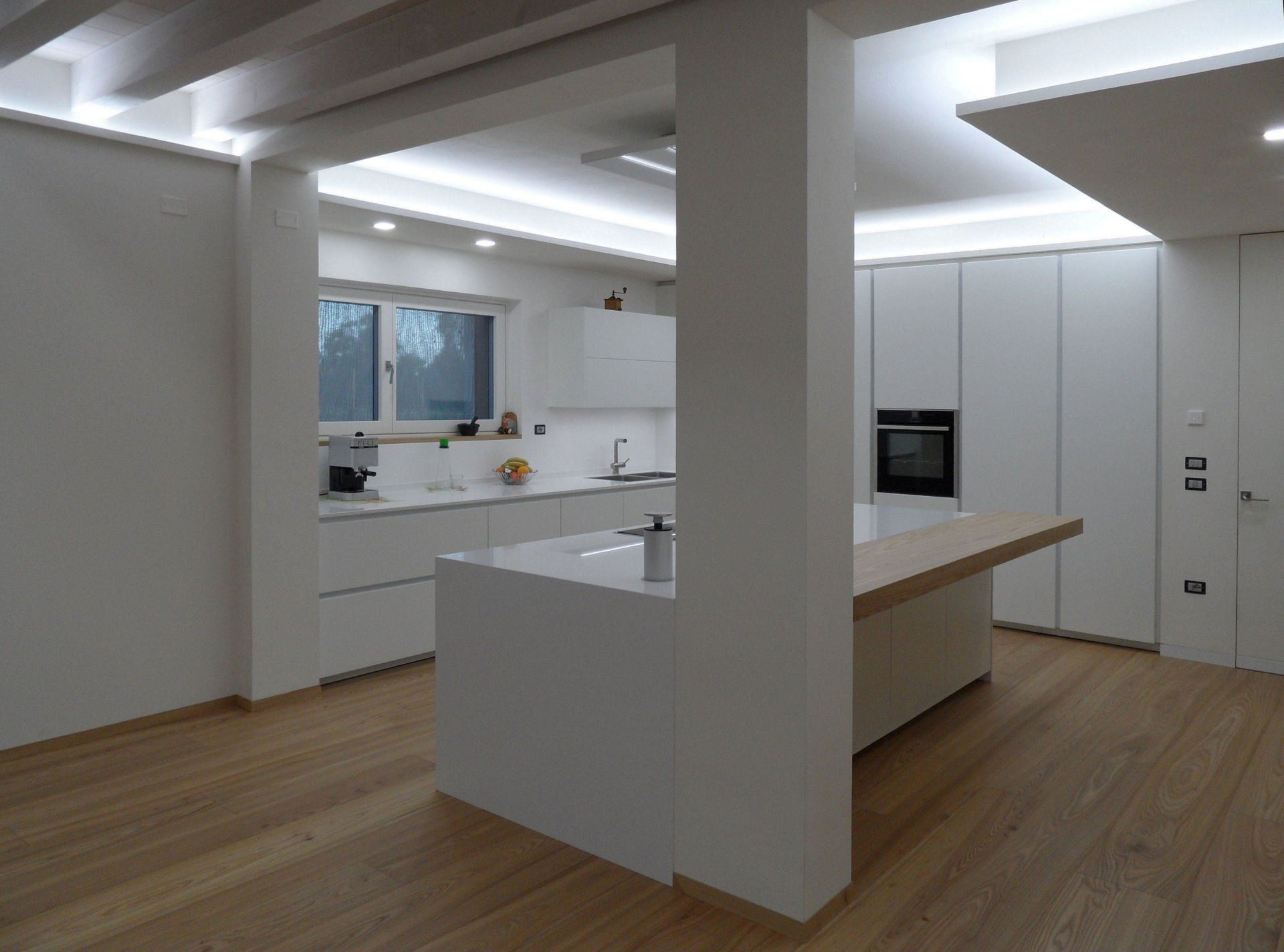 Ambiente cucina con isola dal design moderno bianco opaco su misura artigianale con particolari in rovere naturale