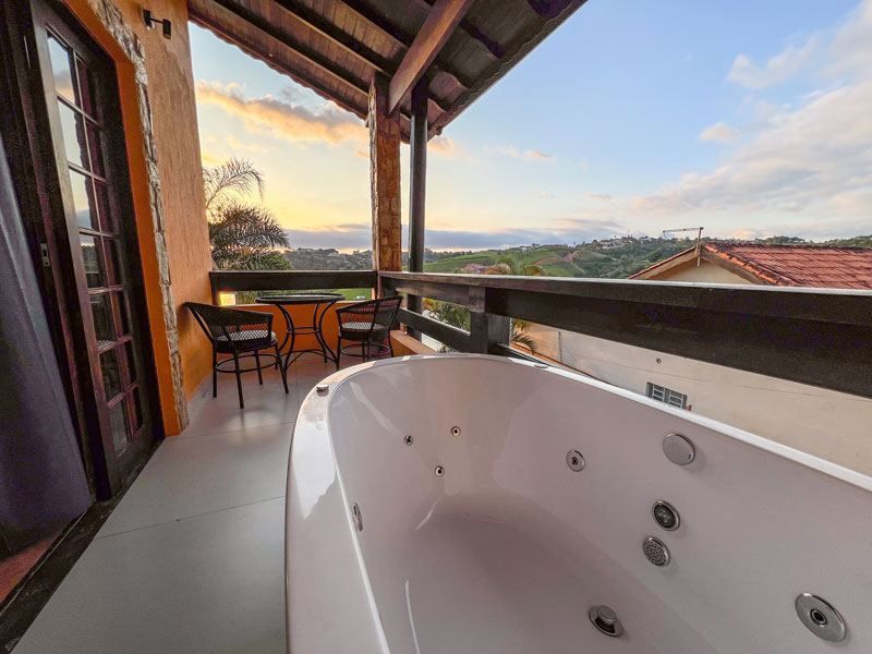 Jacuzzi em uma varanda com mesa e cadeiras, com vista para a paisagem ao pôr do sol.