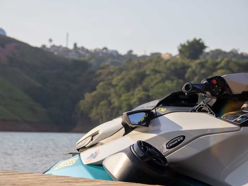 Jet ski branco e azul-turquesa em um píer à beira de um lago, com colinas ao fundo.
