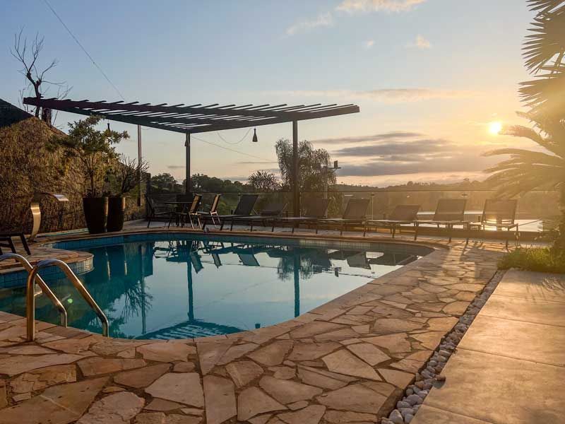 Piscina com espreguiçadeiras, pérgola e vista para o pôr do sol.