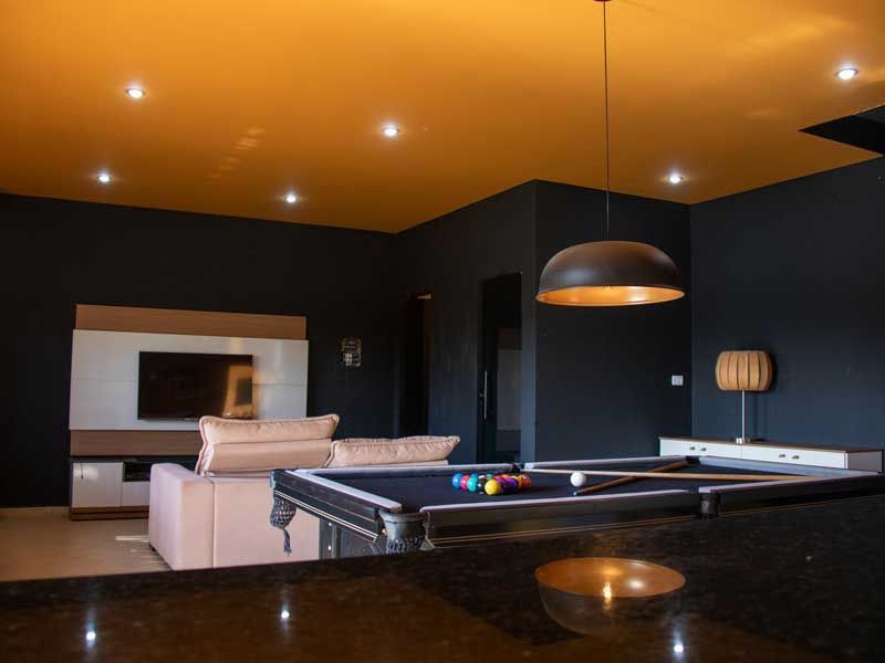 Mesa de bilhar em uma sala escura com teto dourado e iluminação moderna.