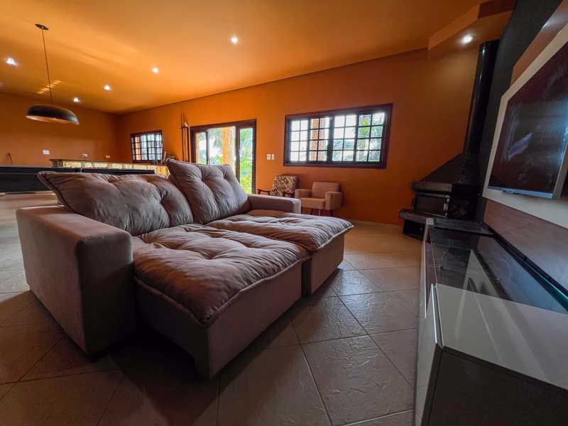 Sala de estar com sofá modular marrom, lareira, janelas e paredes laranja.