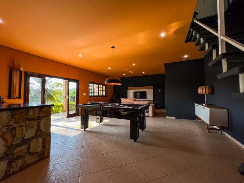 Interior de uma sala de jogos moderna com teto laranja, paredes pretas, mesa de bilhar e vista para o exterior.