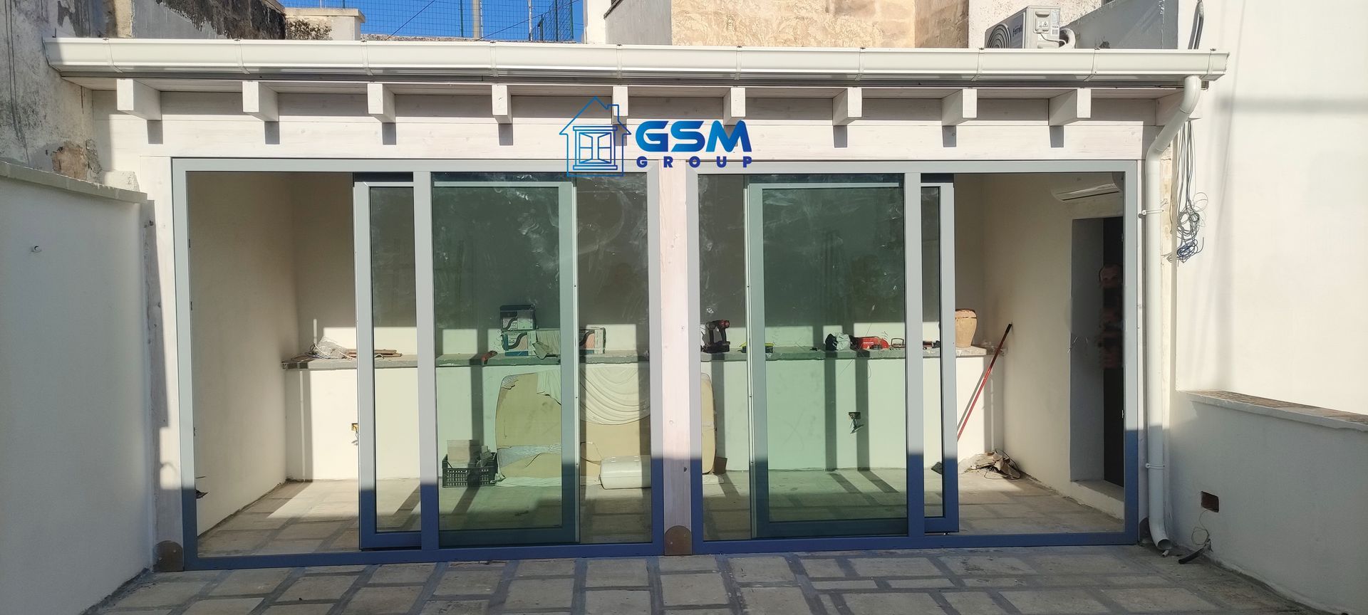 Un'area patio con un tetto a pergola bianco, il logo 