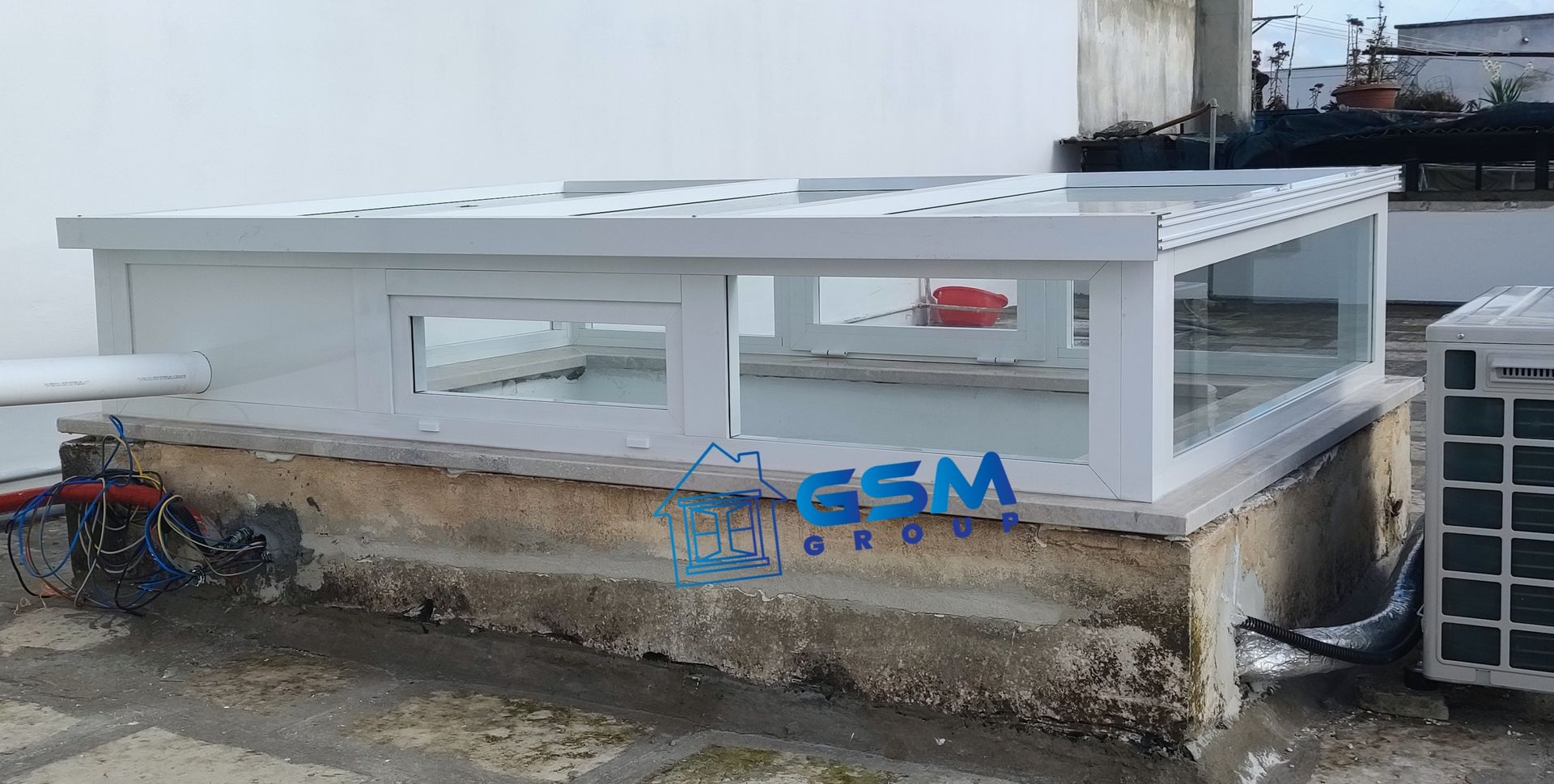 Una struttura rettangolare bianca, racchiusa da pareti in vetro, poggia su una base di cemento sul tetto, accanto a un'unità di condizionamento dell'aria.