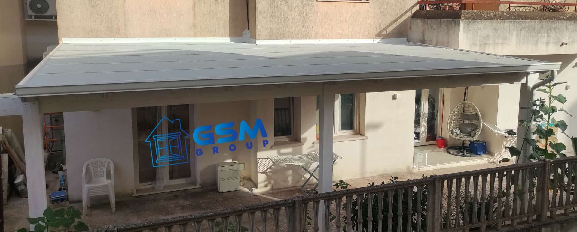 Una struttura bianca per la copertura del patio esterno, annessa a una casa beige, con il logo aziendale sovrapposto al centro.