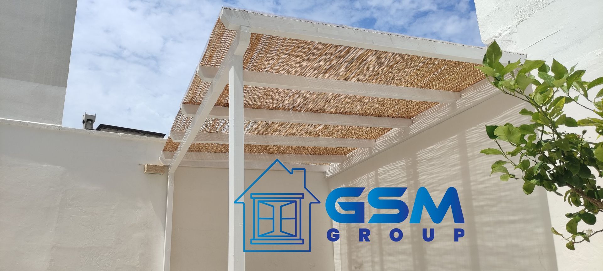 Una pergola bianca con tetto di paglia e canne si erge addossata a una parete bianca con il logo del Gruppo GSM sovrapposto al centro.