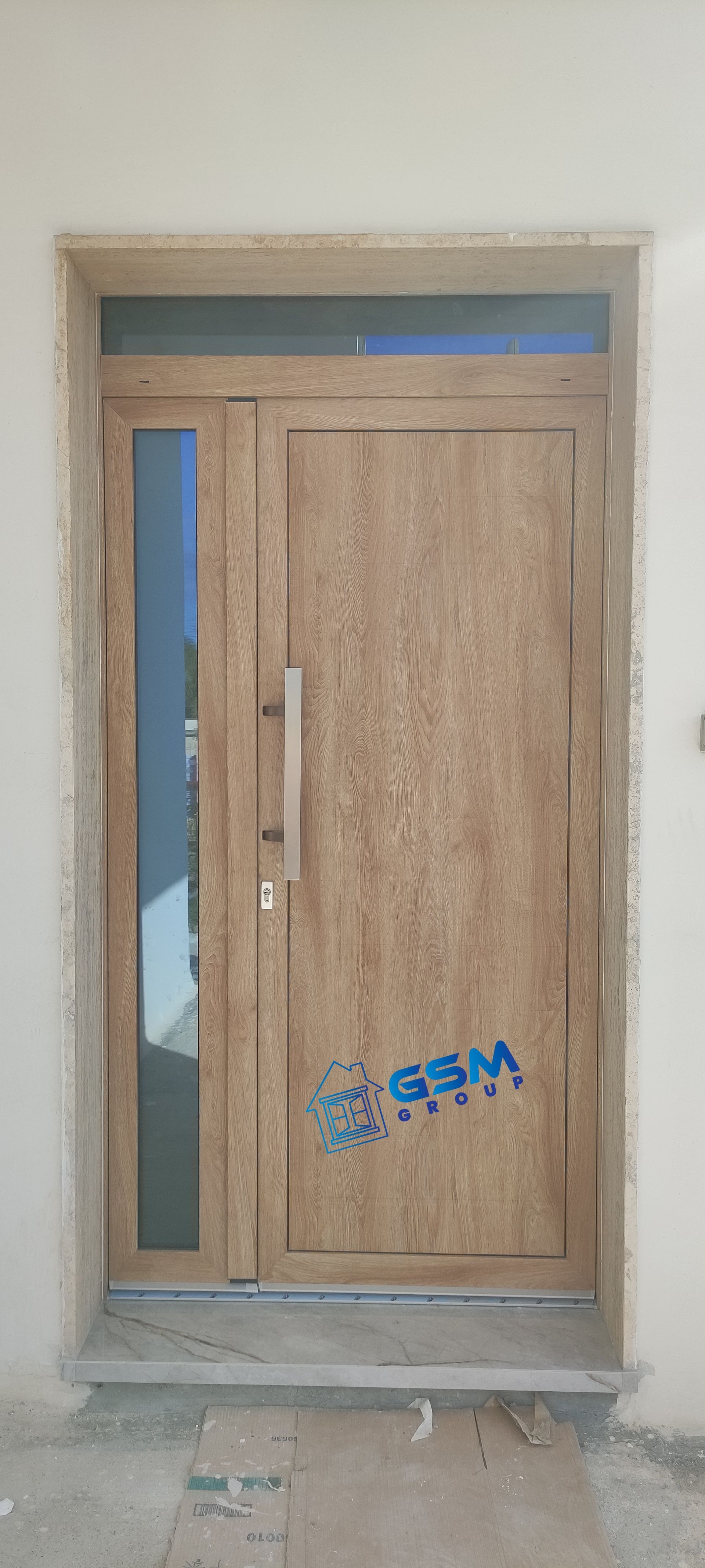 Una moderna porta d'ingresso con finitura effetto legno, dotata di un pannello laterale verticale in vetro e una lunga maniglia rettangolare in metallo, incastonata in una parete chiara.