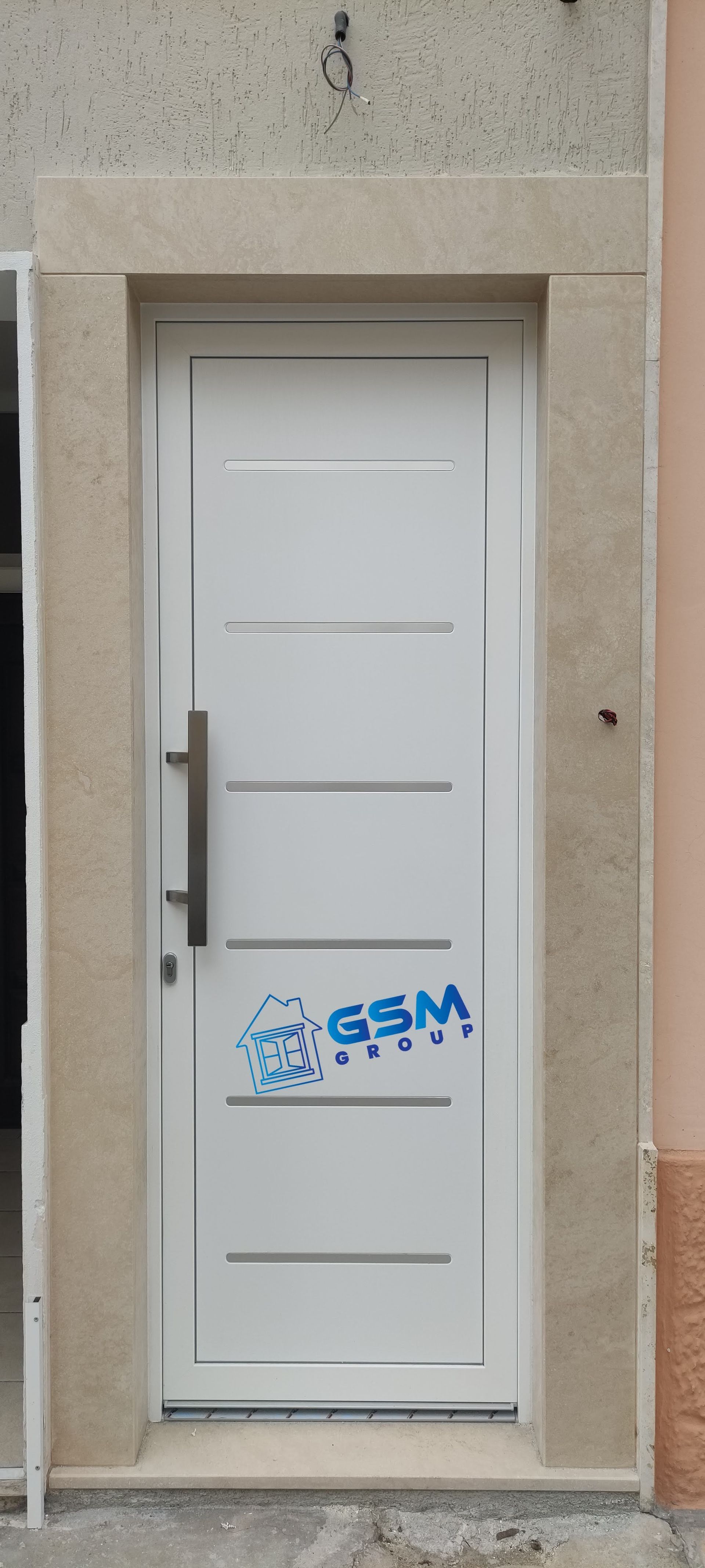 Una porta moderna bianca con maniglia lunga e pannelli orizzontali, incastonata in una cornice di pietra chiara sulla facciata di un edificio.