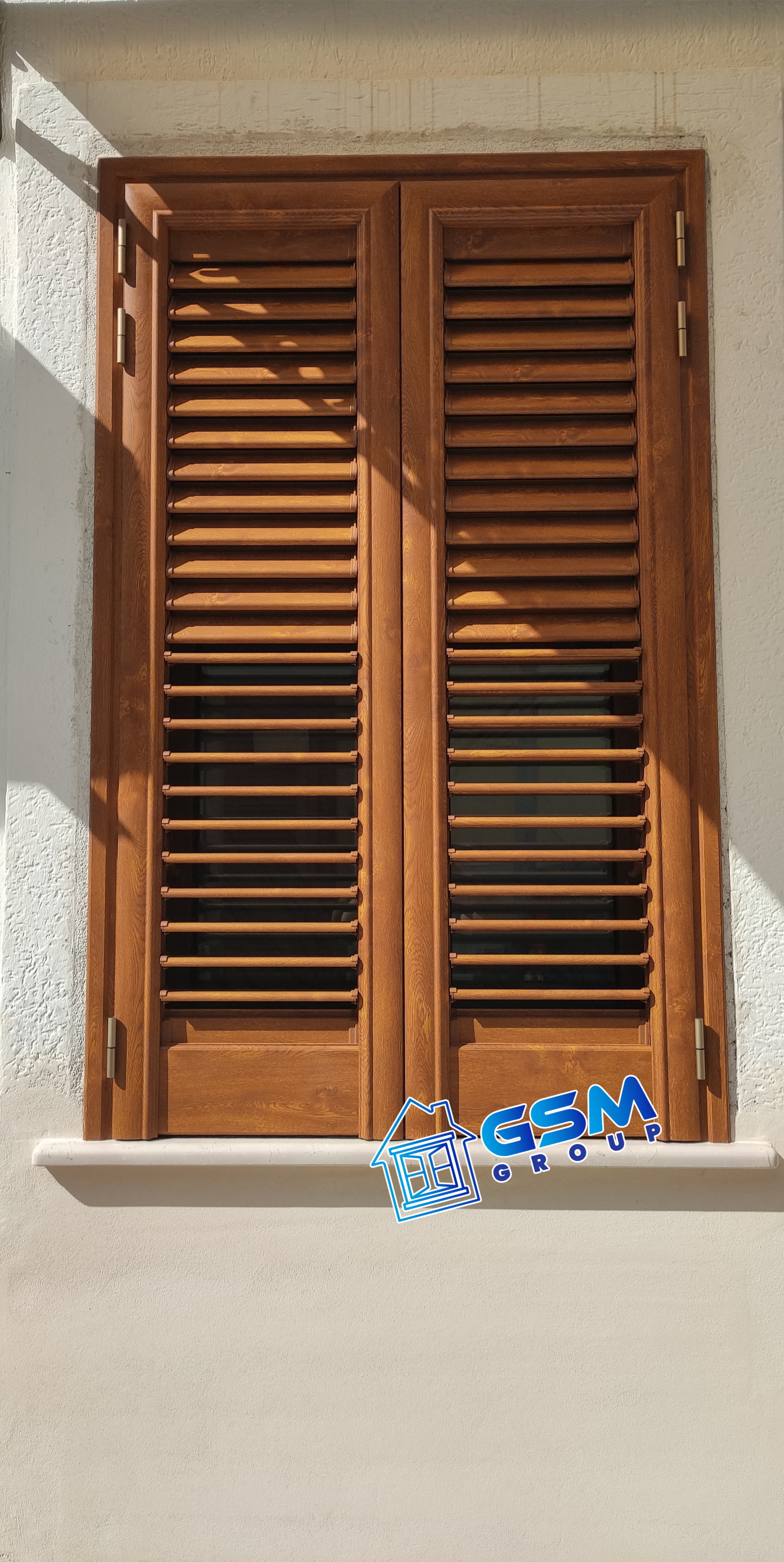 Persiane bianche a stecche inserite in una cornice su una parete esterna.