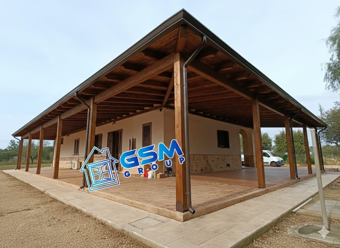 Una casa a un solo piano con un'ampia veranda coperta in legno che avvolge l'esterno, caratterizzata da una base rifinita in pietra.