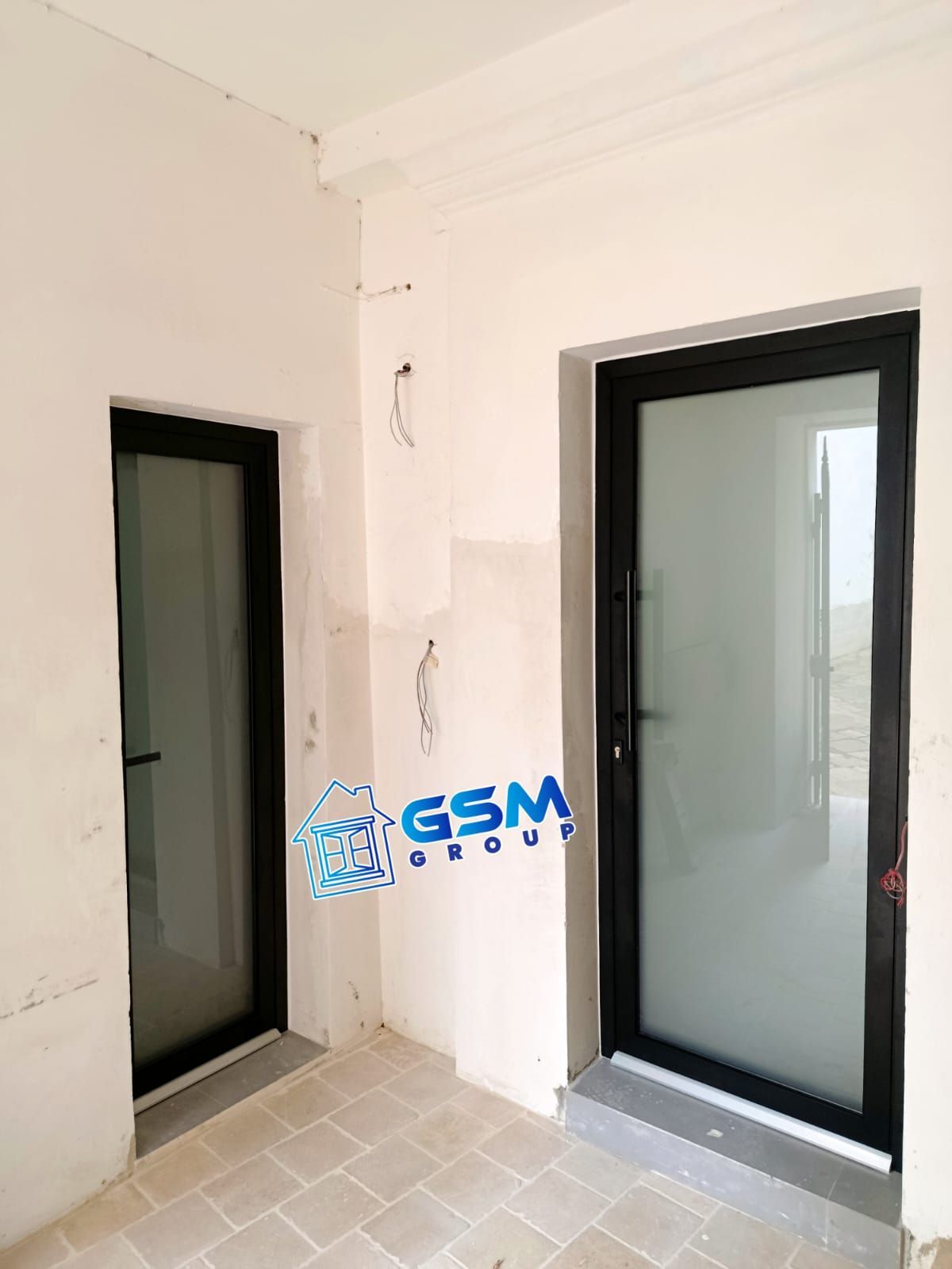 Due porte a vetri con cornice nera incastonate in una parete interna non rifinita con pavimento in piastrelle chiare e logo blu del Gruppo GSM.
