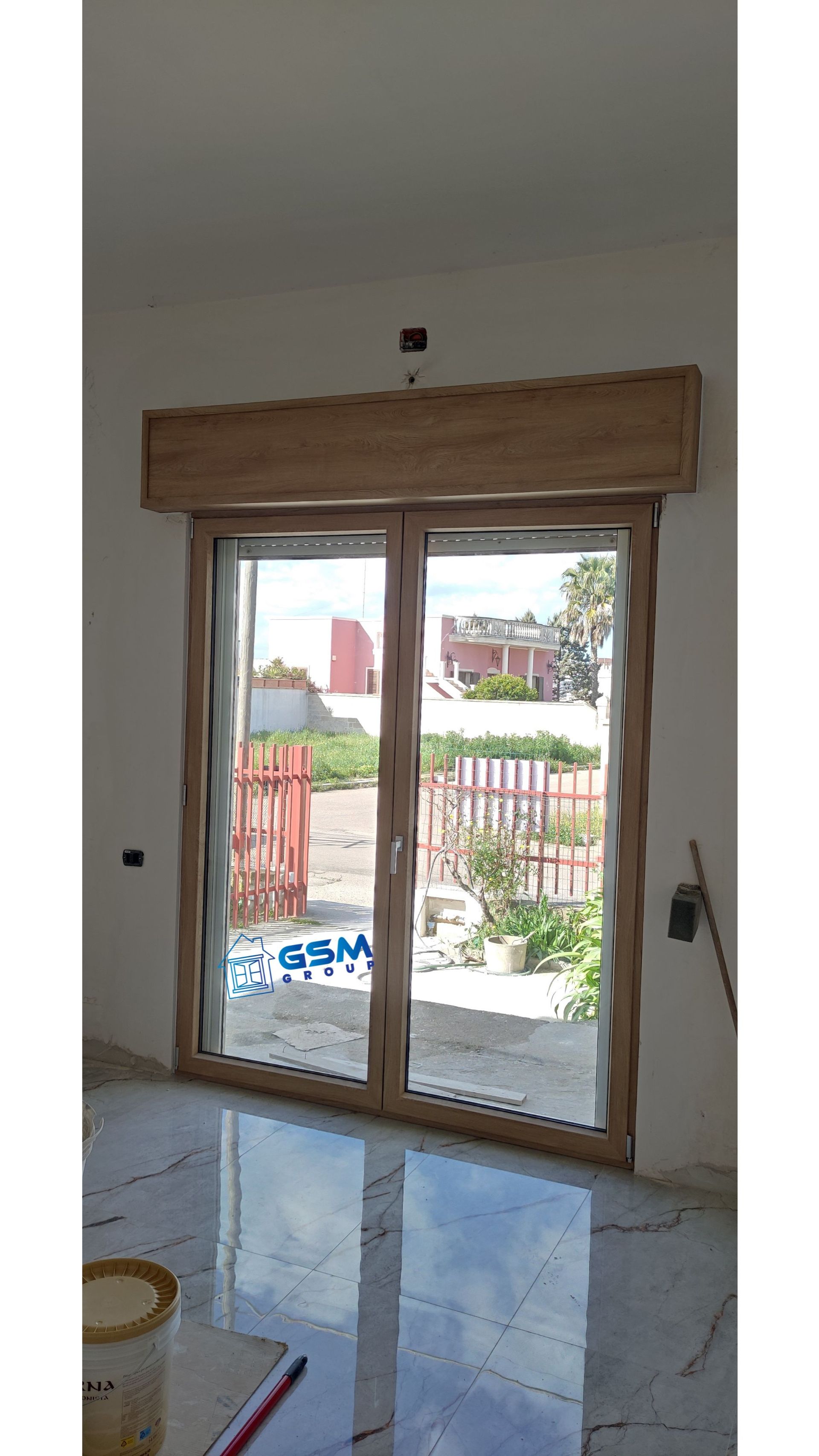 Una coppia di porte a vetri con telaio in legno e cassonetto superiore coordinato, installate in una stanza con pavimento in piastrelle di colore chiaro.