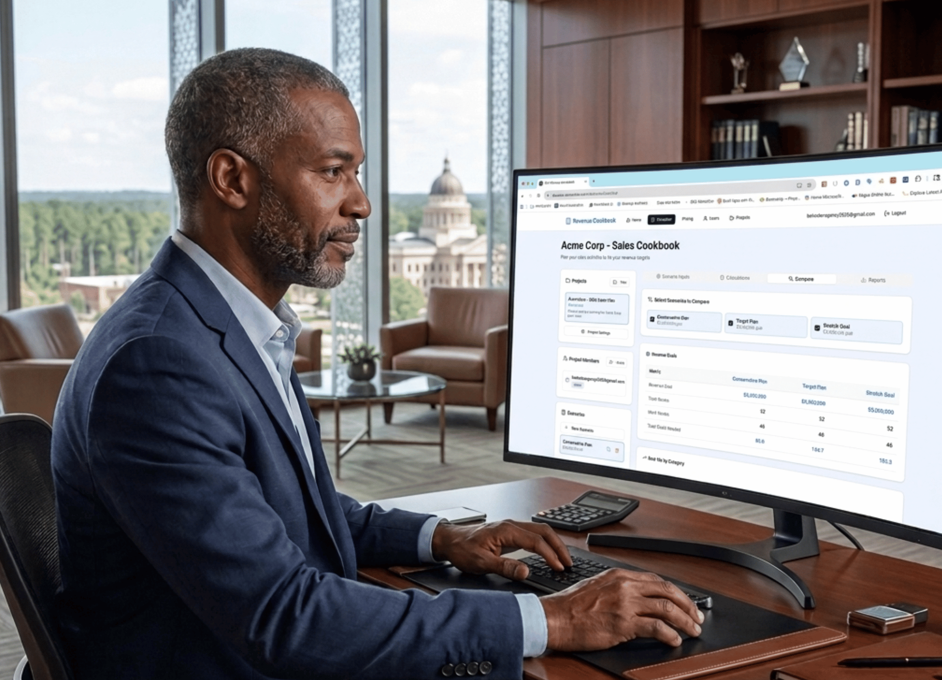 A professional working at a computer in a modern office with a view of a capitol building through a large window.