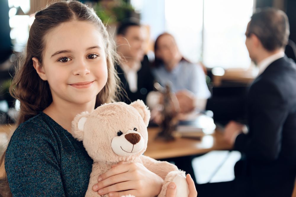 A little girl is holding a teddy bear in front of a family.