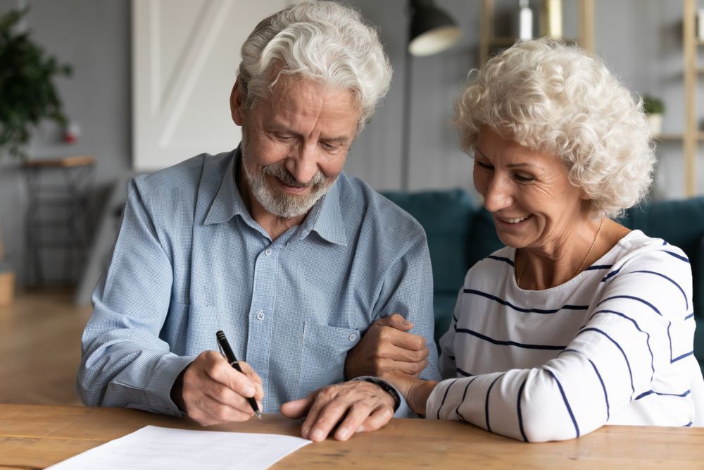 An elderly couple is sitting at a table signing a document.