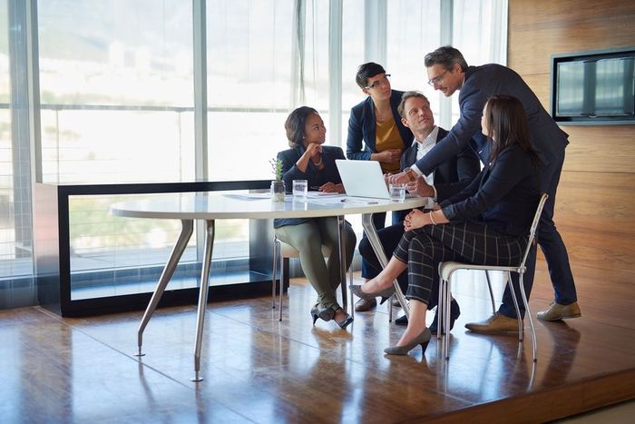 A group of people are sitting around a table looking at a laptop.