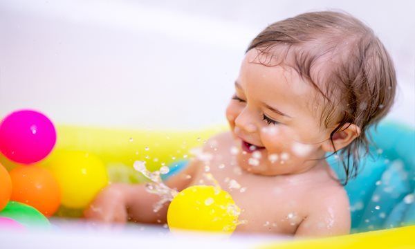 Baby laughing in a colorful bathtub, splashing water with plastic balls.