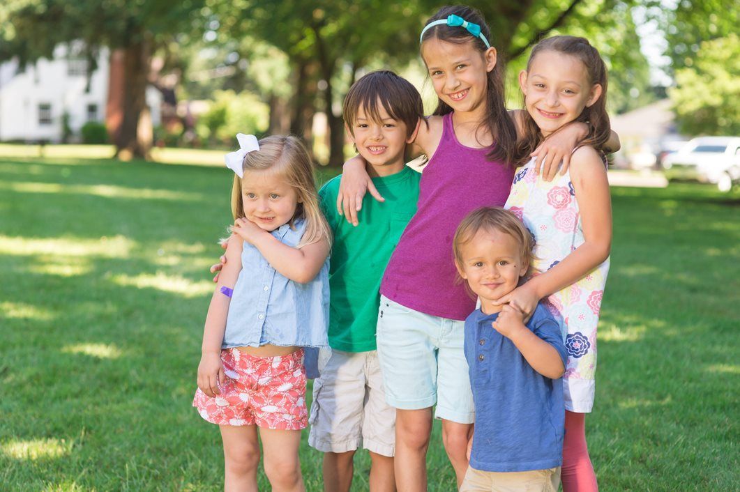 Children smiling and embracing in a grassy park, trees in the background, sunny day.