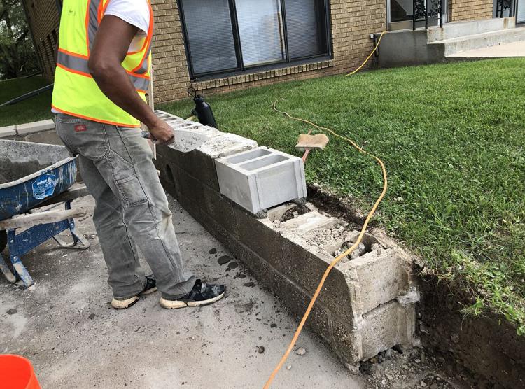 A man in a yellow vest is working on a concrete wall