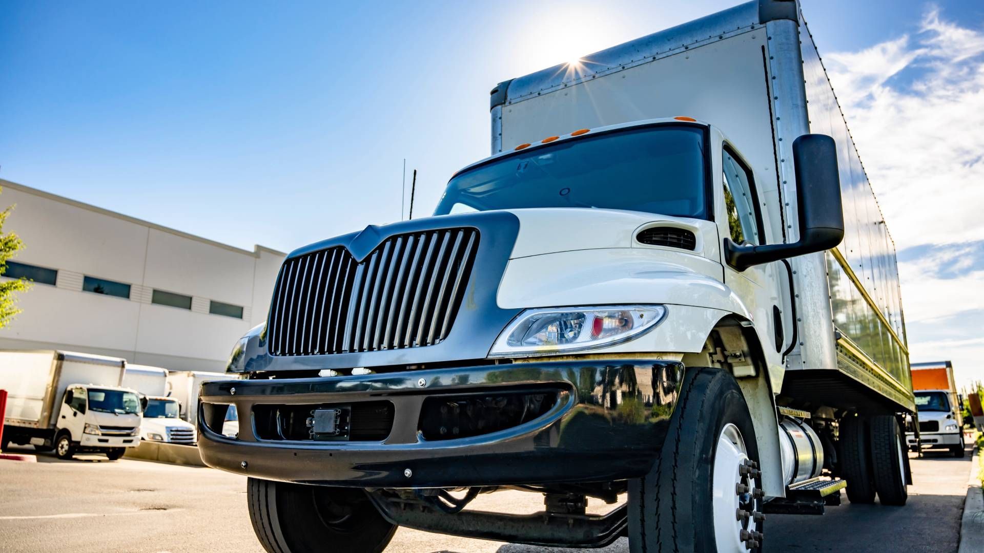 White delivery truck parked in front of a warehouse on a sunny day.