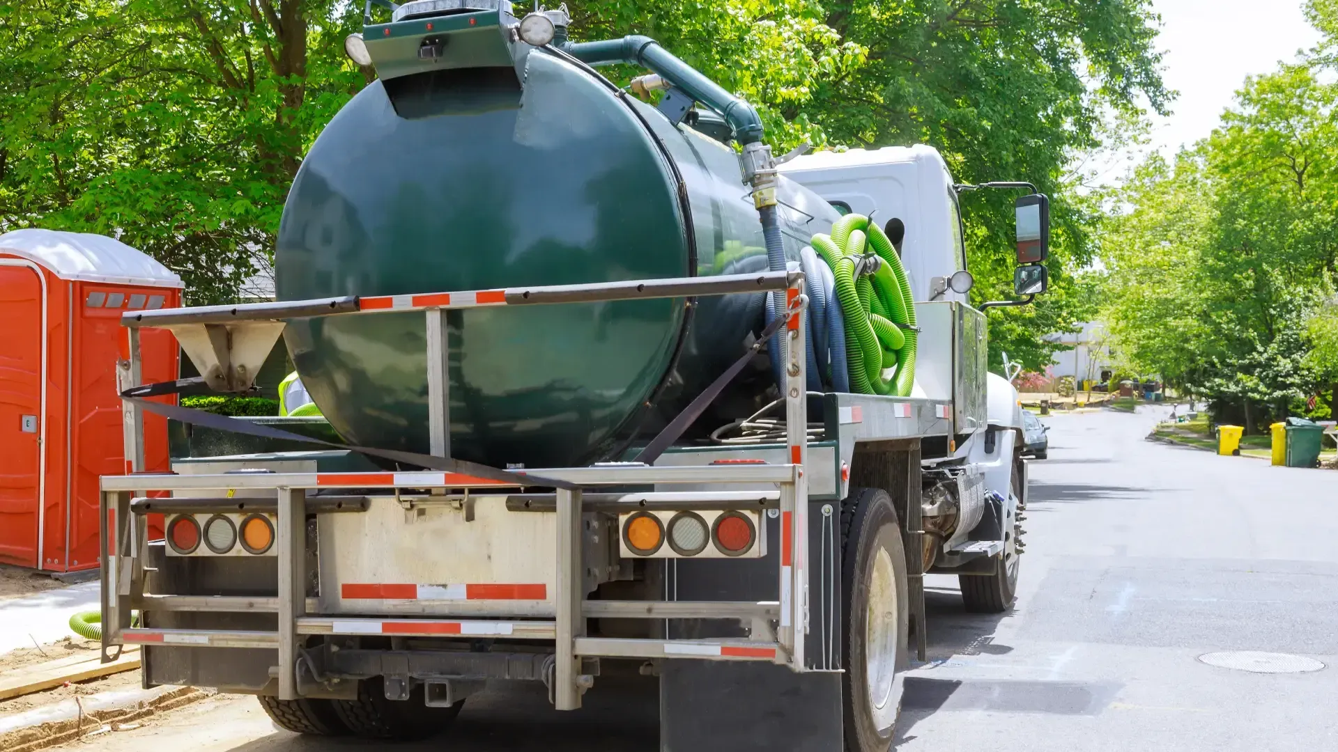 Rear view of a septic truck with a green tank parked next to a construction site.
