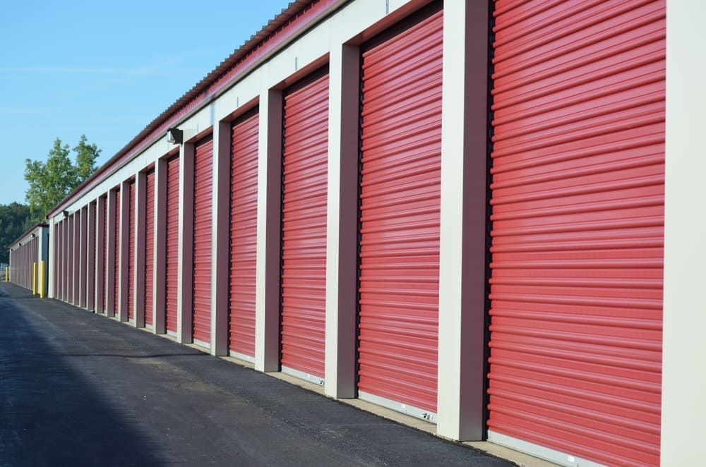 Row of red storage unit doors with white trim and asphalt driveway.