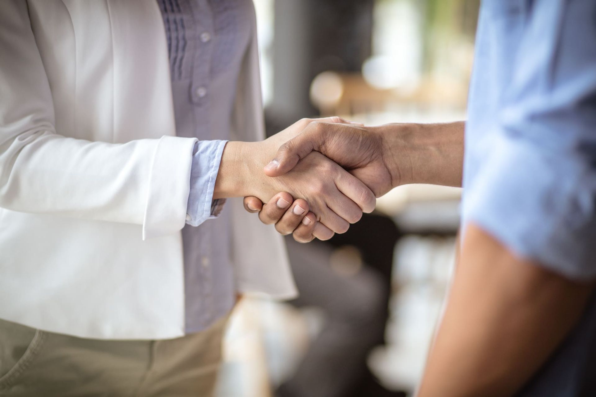 Person in white blazer shakes hands with a person in blue shirt, likely a business agreement.