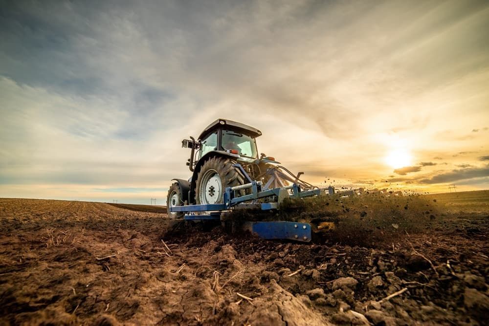 Tractor plowing a field at sunset, kicking up dirt.