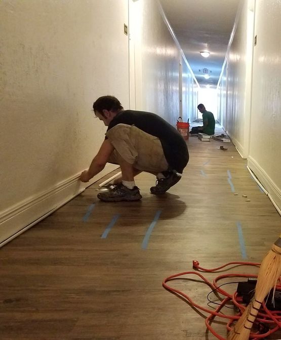 A man is kneeling down in a hallway installing LVP. 