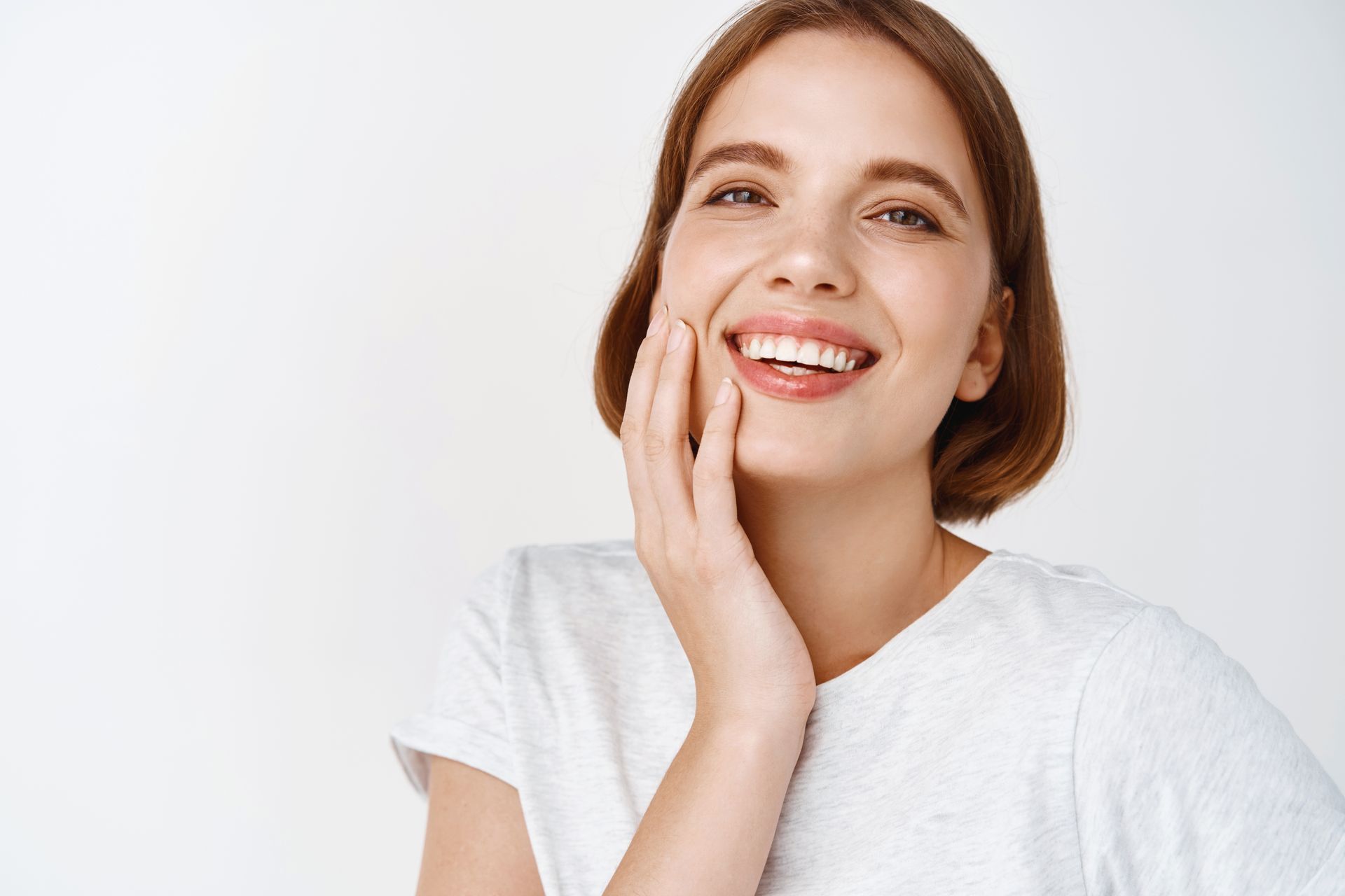A woman is smiling and touching her face with her hand.
