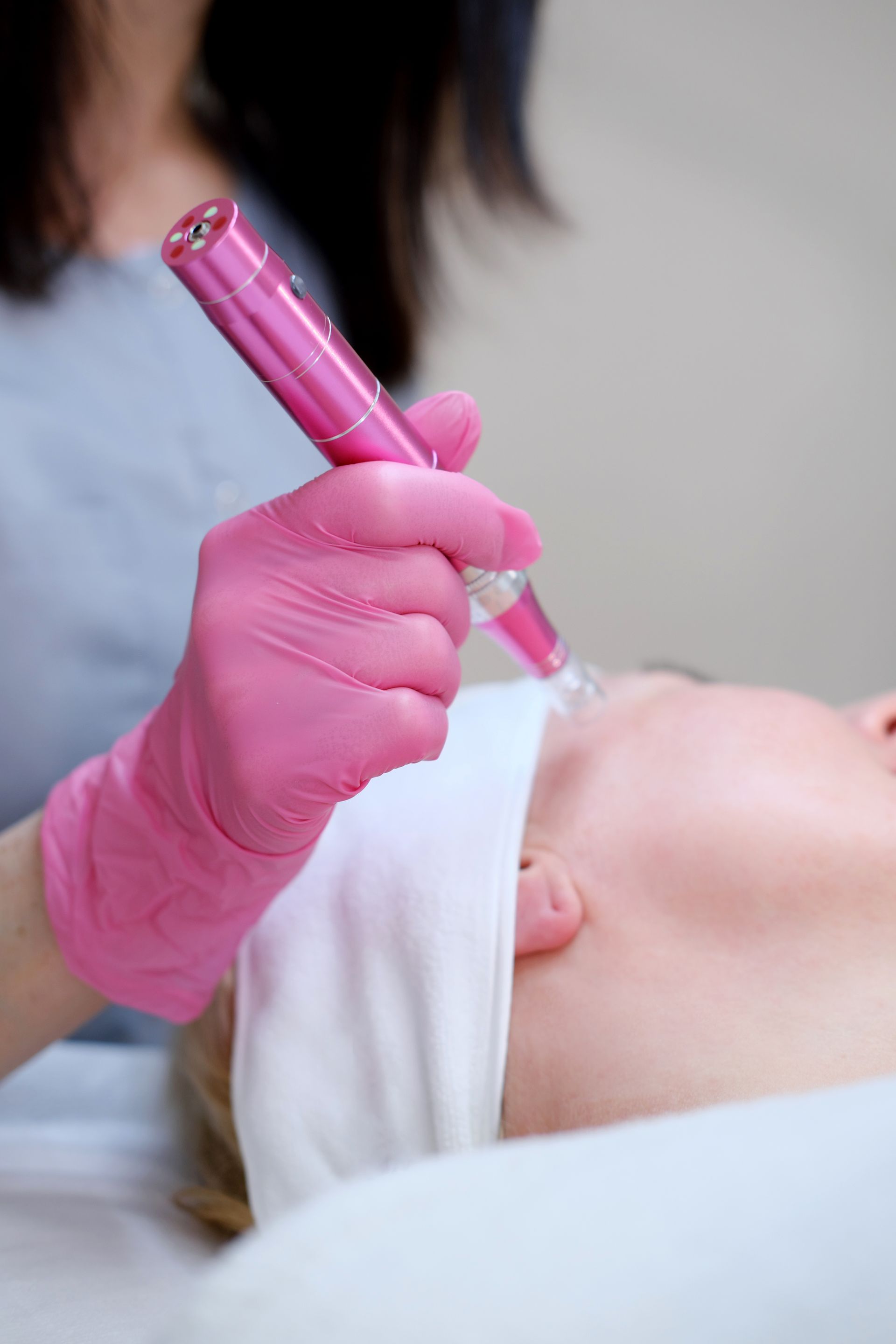 A woman in pink gloves is holding a pink pen over a woman 's face.