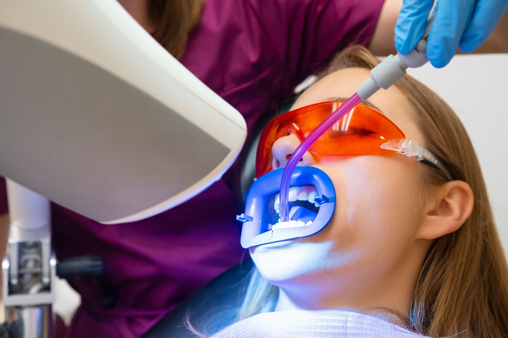 A woman is getting her teeth whitened by a dentist.