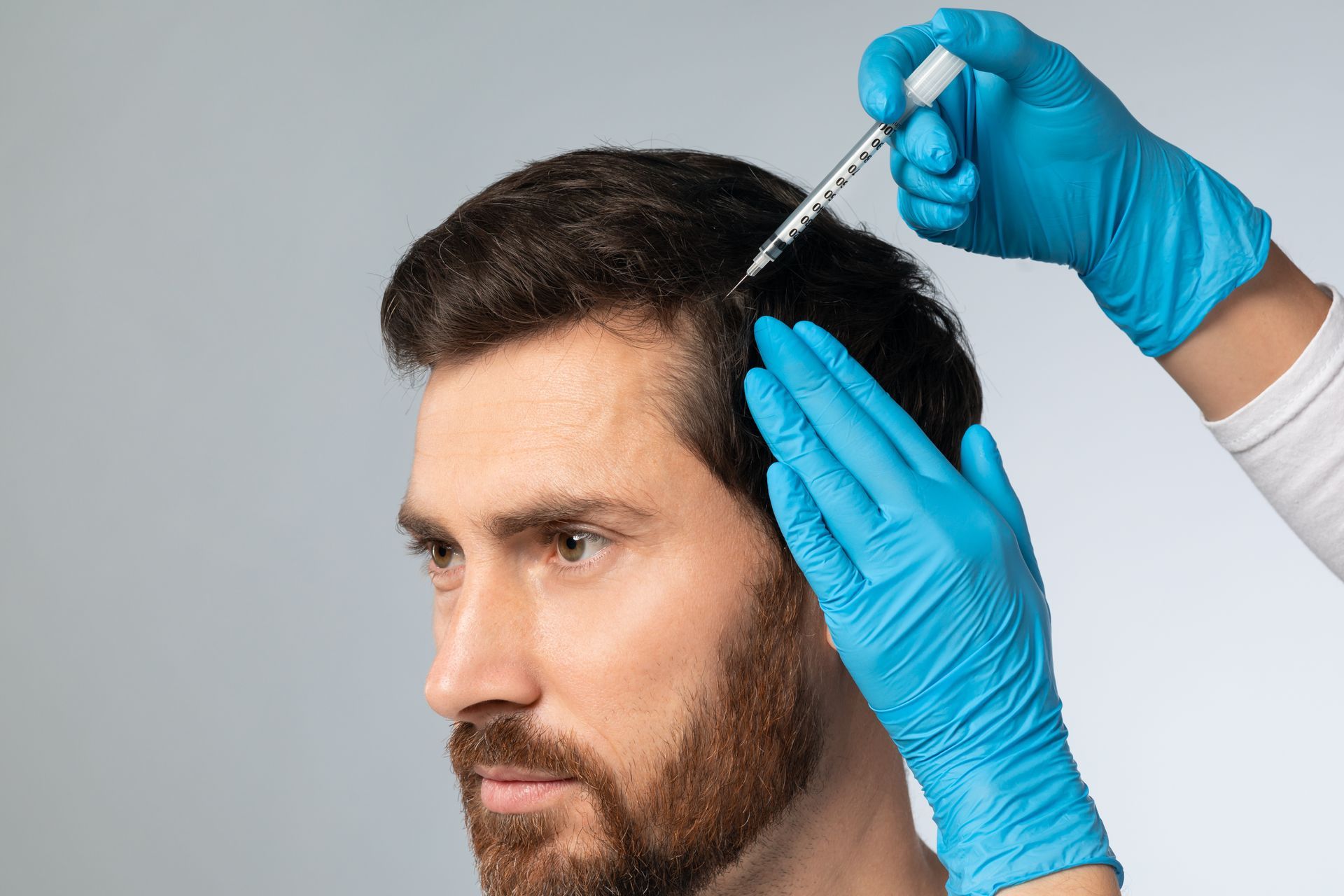 A man with a beard is getting an injection in his hair.