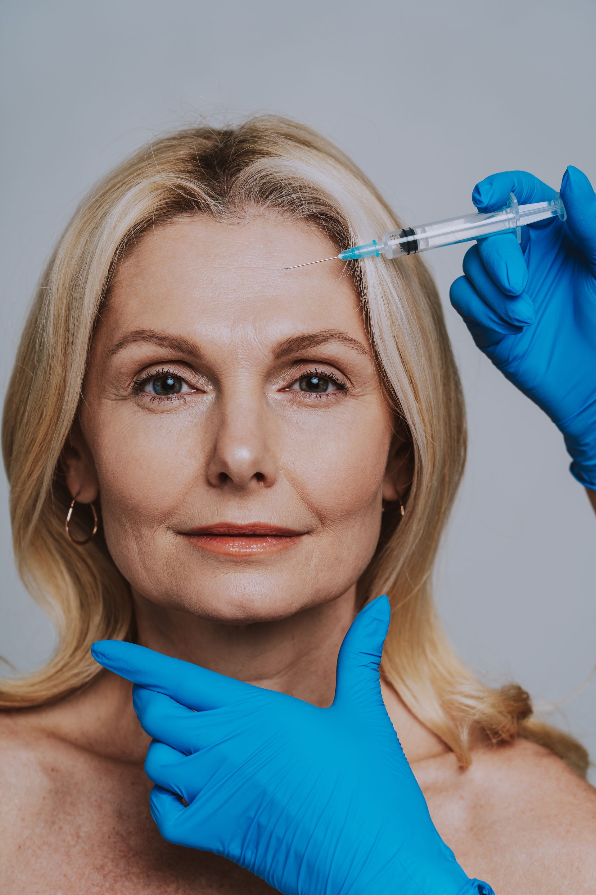 A woman is getting a botox injection in her forehead.