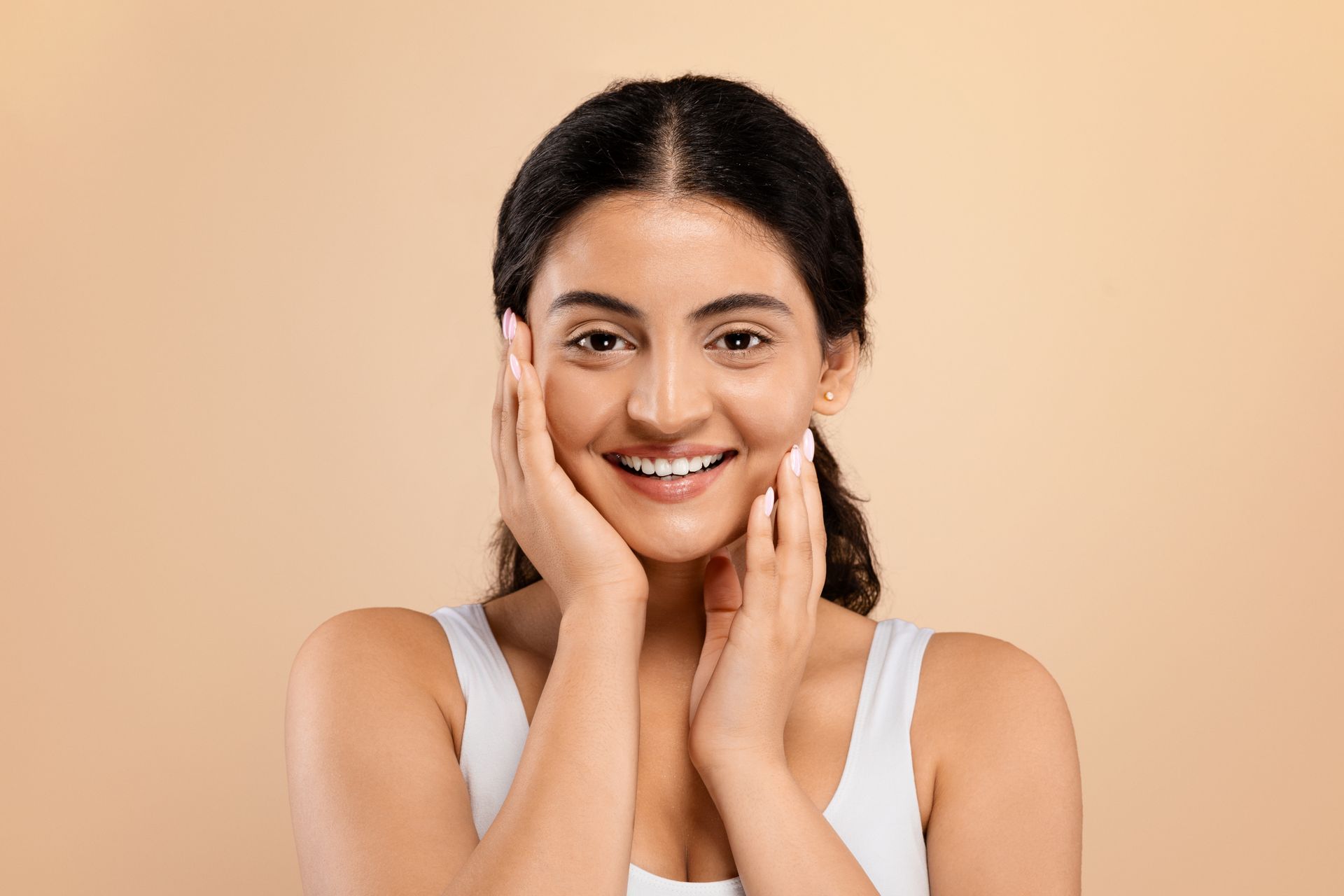 A woman is smiling and touching her face with her hands.