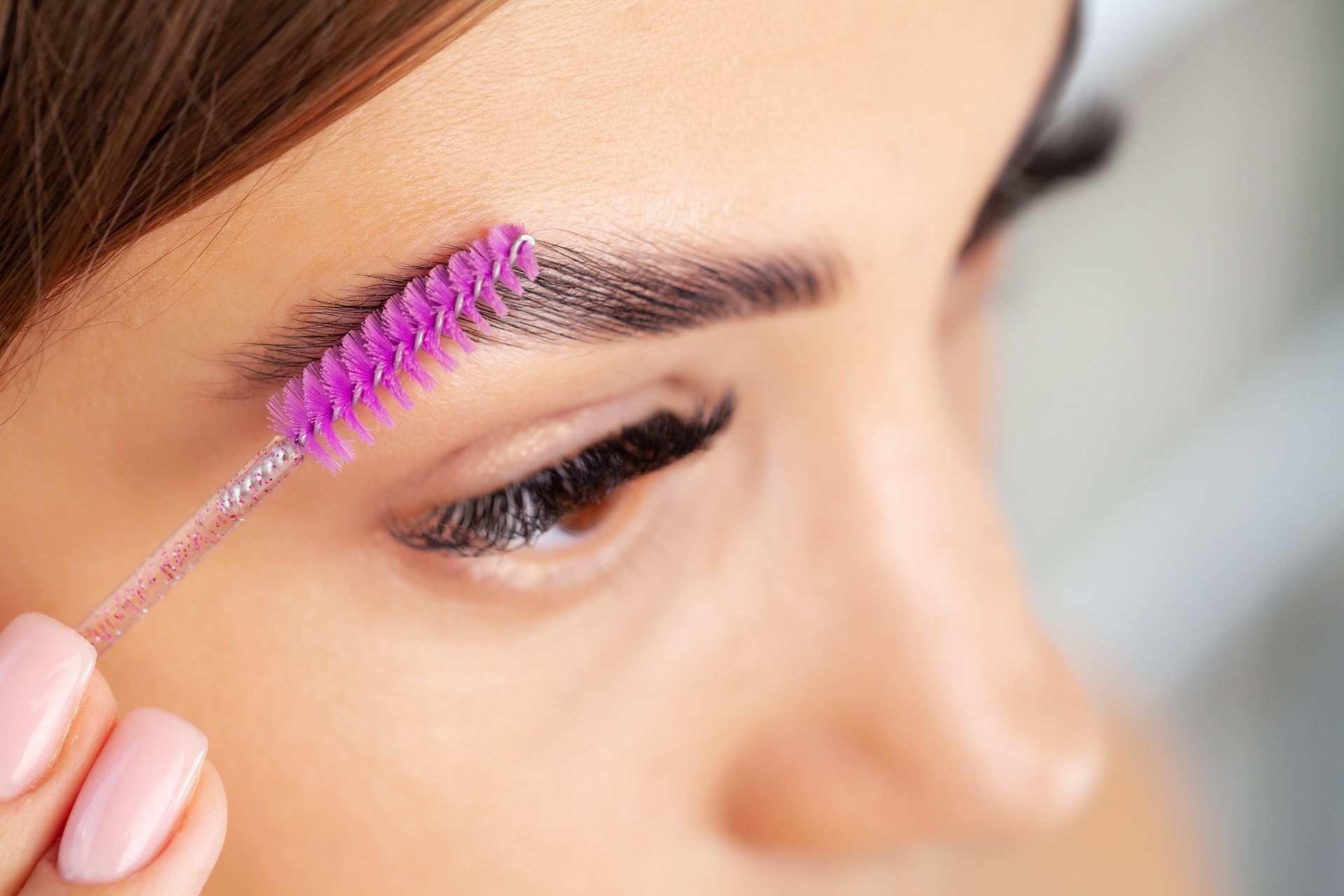 A woman is brushing her eyebrows with a purple brush.