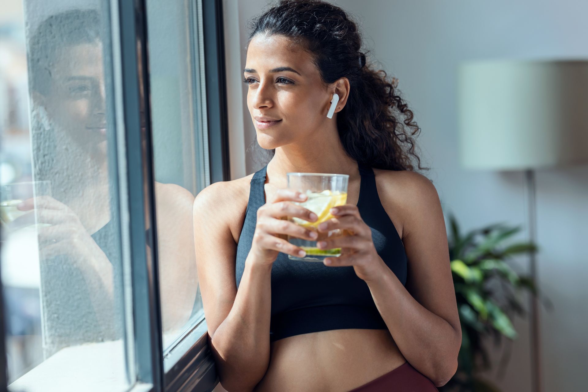 A woman is holding a glass of lemonade and looking out of a window.