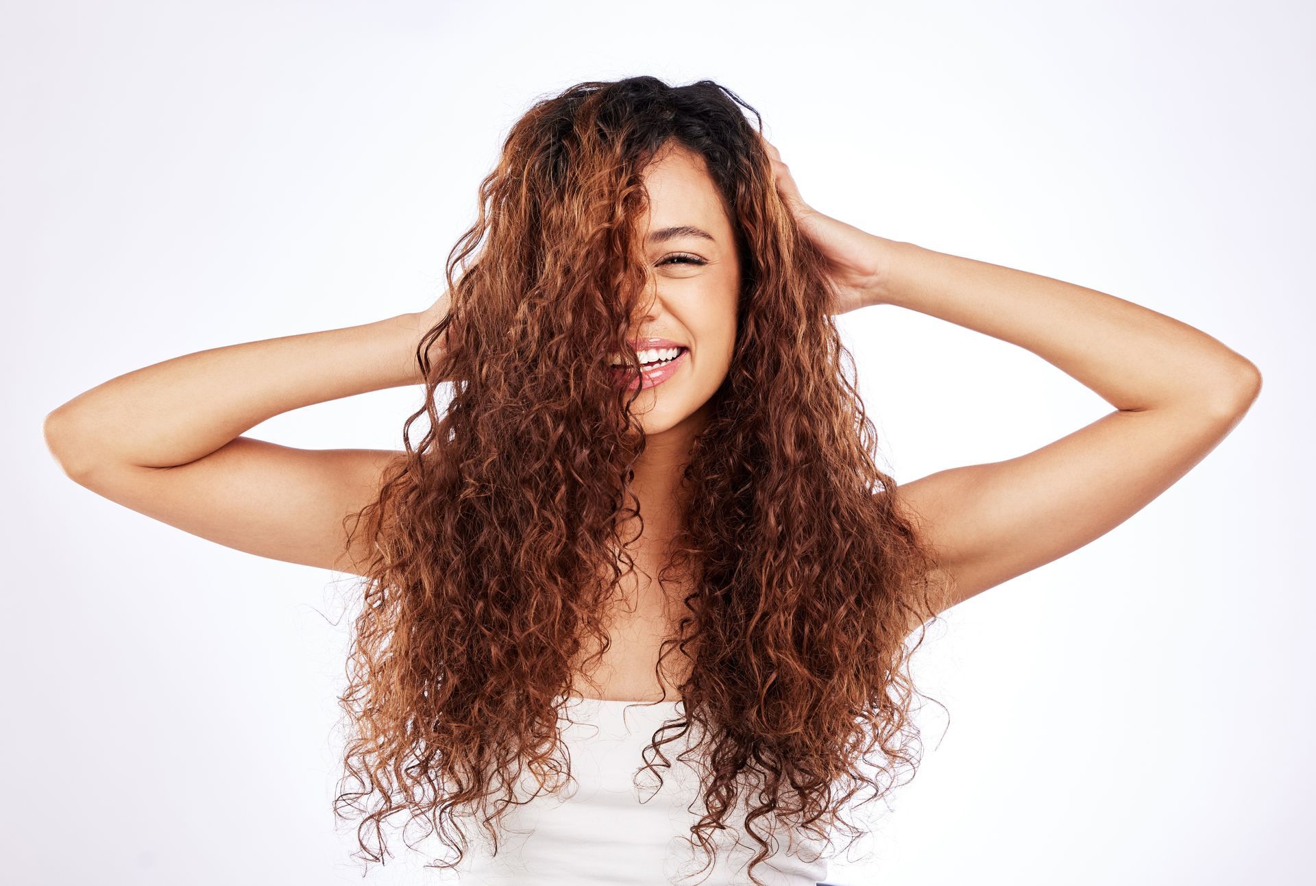 A woman with long curly hair is smiling and holding her hair.