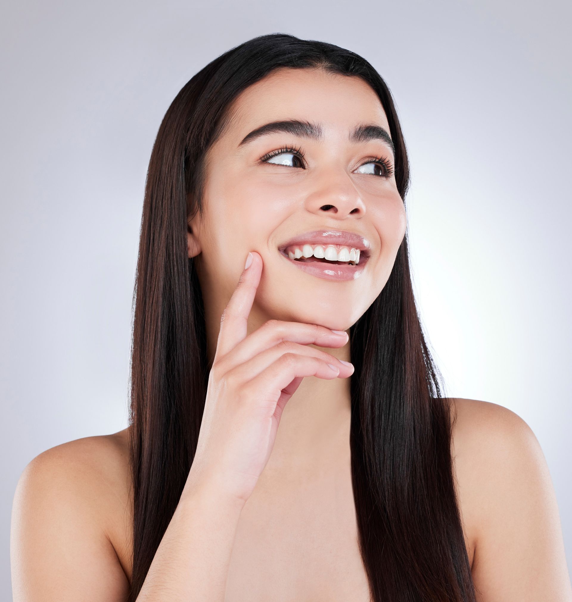 A woman with long hair is smiling with her hand on her chin