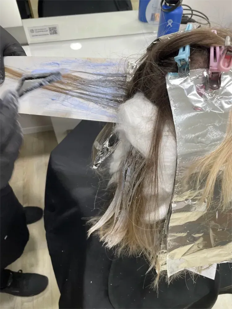 Eine Friseurin färbt in einem Salon Haare mit Foliensträhnen.