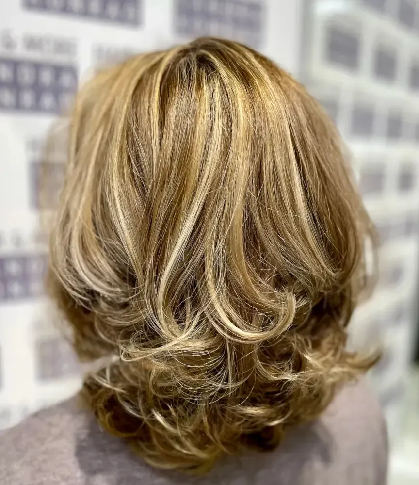 Schulterlanges blondes Haar mit Strähnchen, gestylt mit Locken und Stufen.