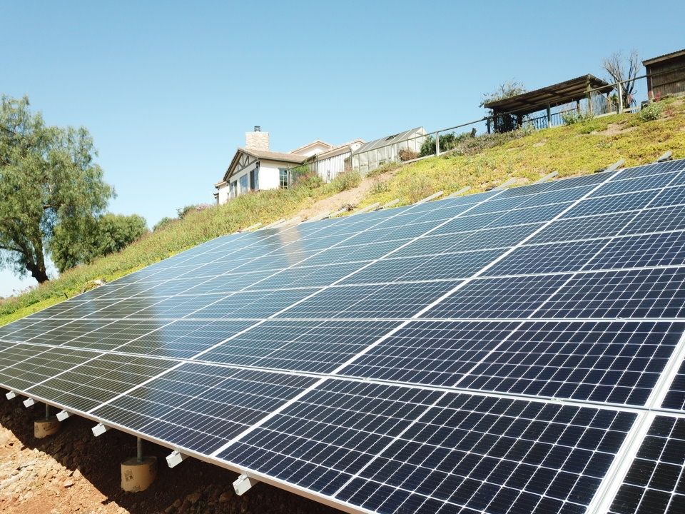 A solar panel island on a hillside with a house in the background.