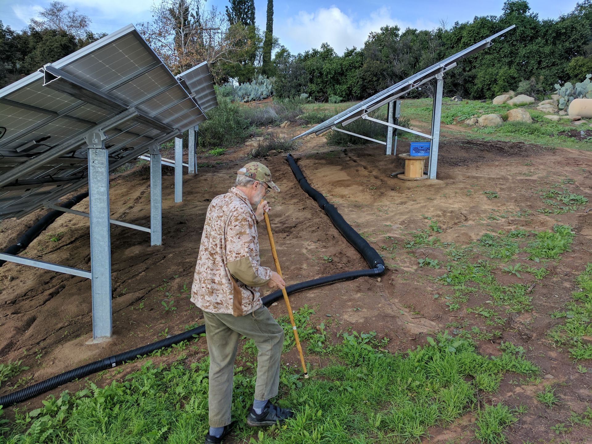 A man is standing in a field next to a solar panel.