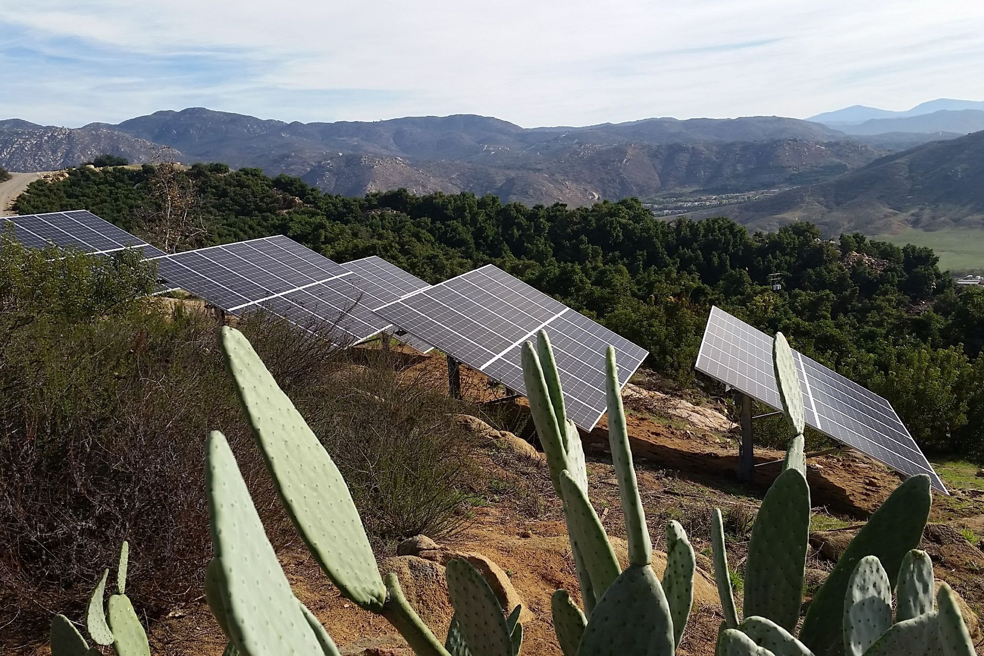 A row of solar panels on top of a hill with mountains in the background
