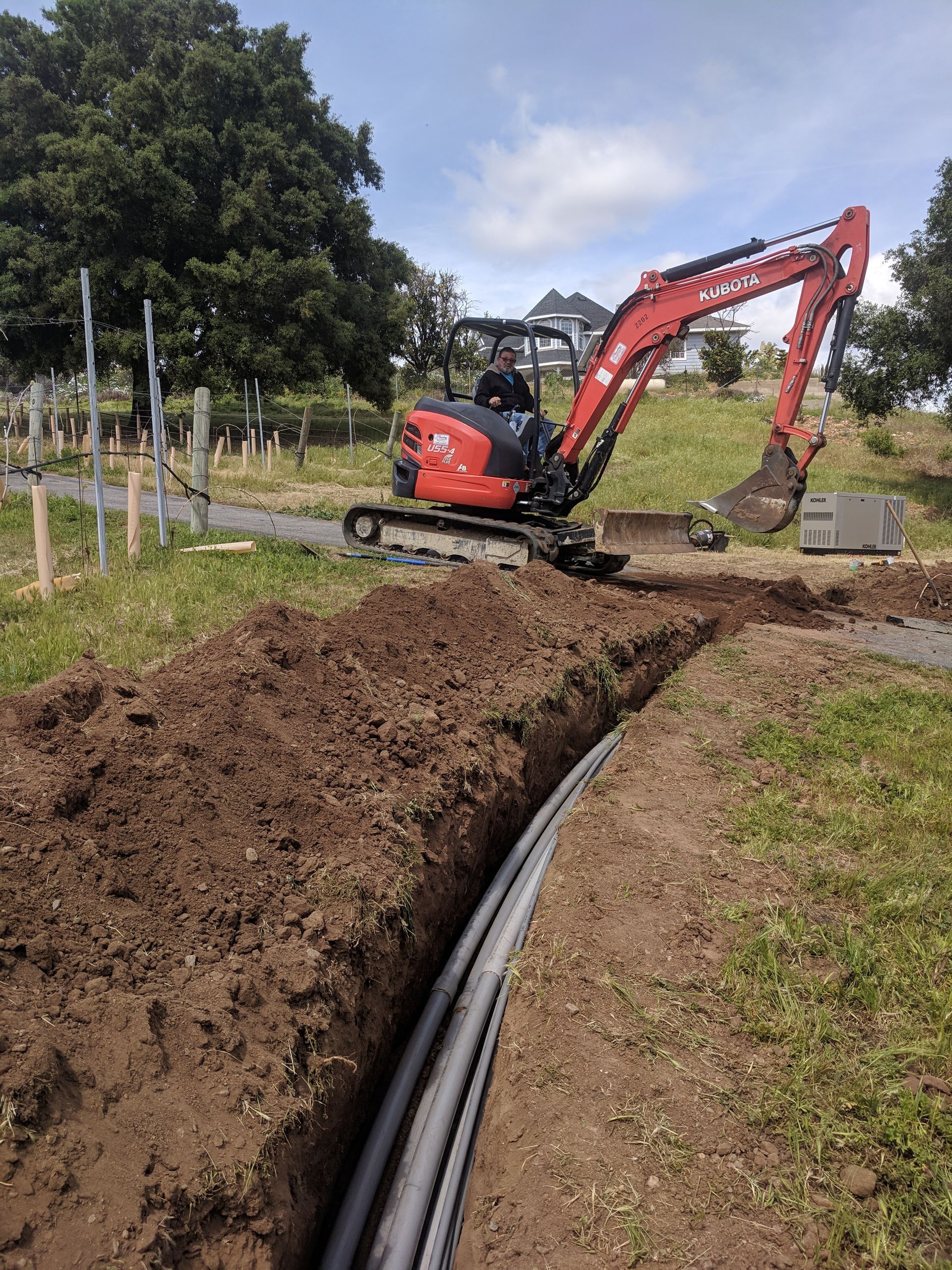 A red and black excavator is digging a hole in the ground.