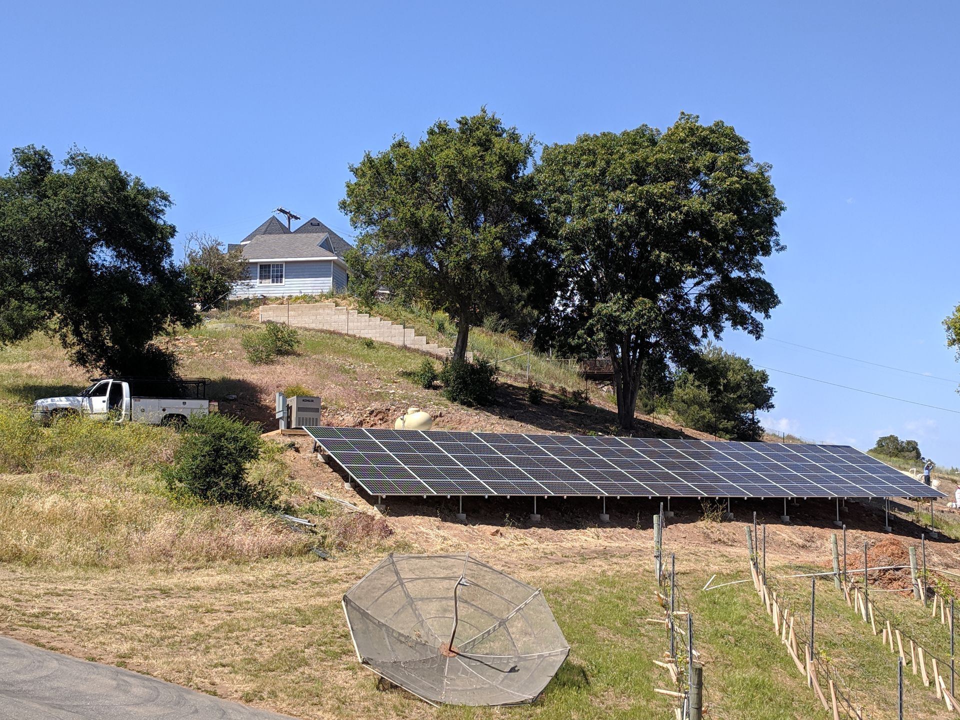 A row of solar panels on a hillside with a house in the background