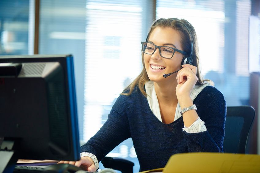 A woman wearing a headset is sitting in front of a computer.