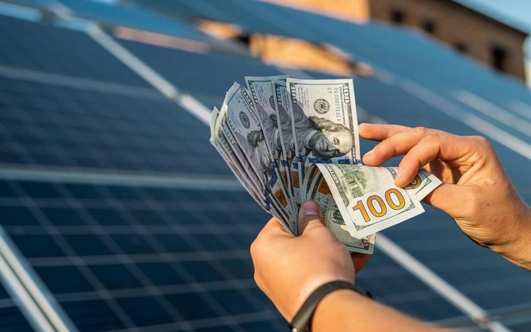 A person is holding a fan of money in front of a solar panel.